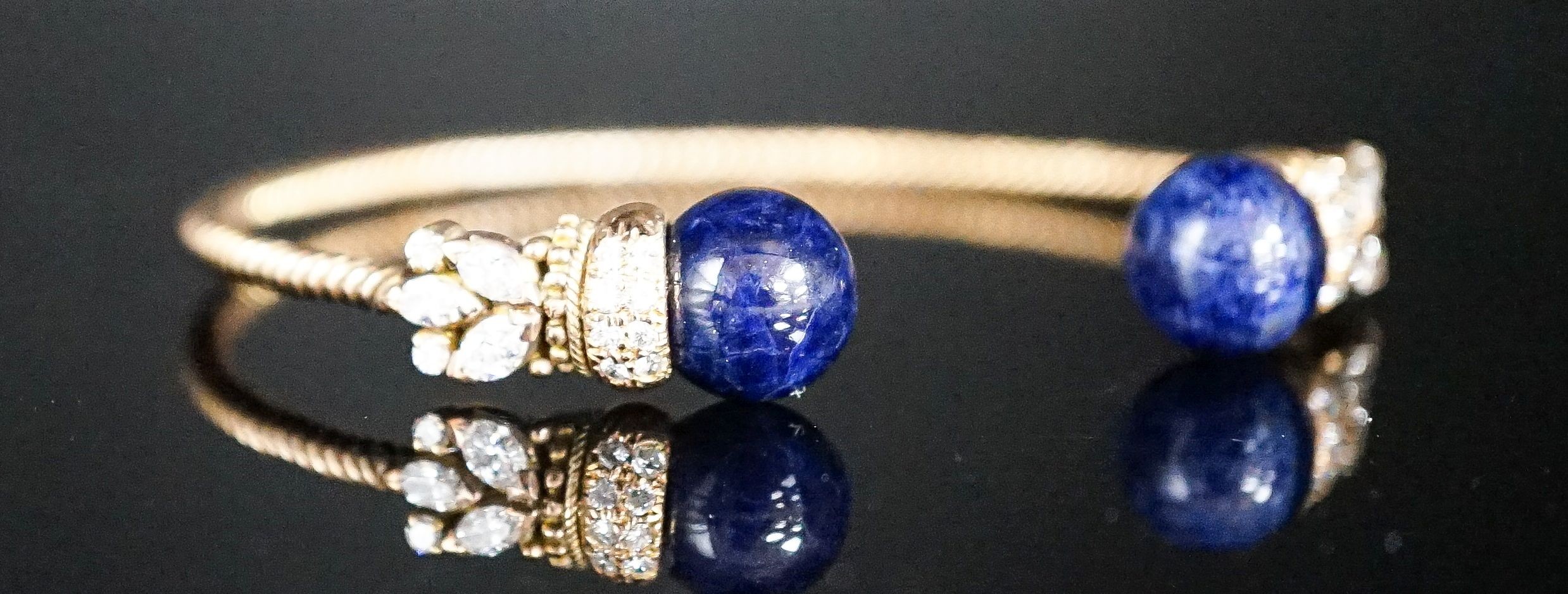 A modern yellow metal twist, two stone sodalite? and diamond set open bangle, gross weight 14 grams.